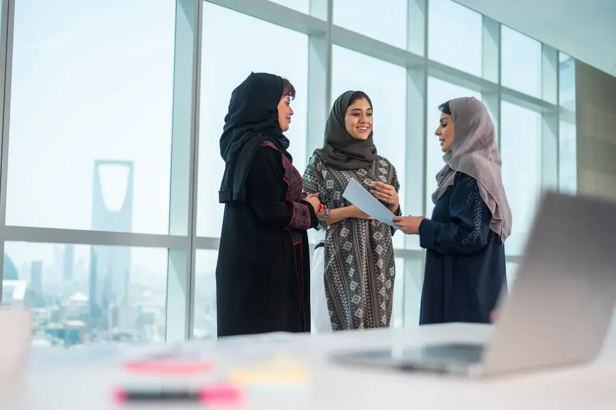 ثلاث رائدات أعمال يتناقشن حول مشروع في مكتب يطل على أفق الرياض